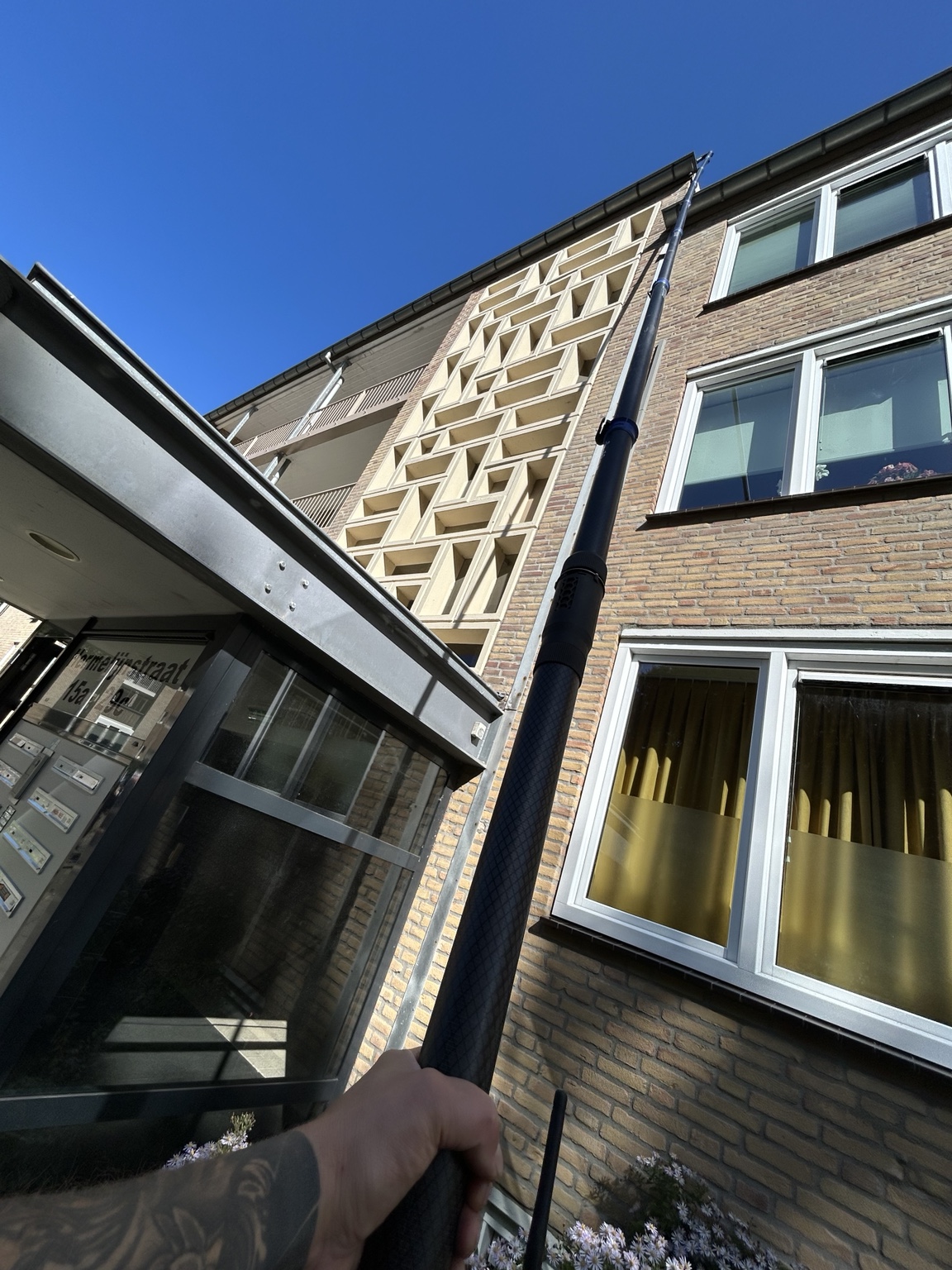 Telescoopstok tegen een blauwe lucht bij een hoge woning