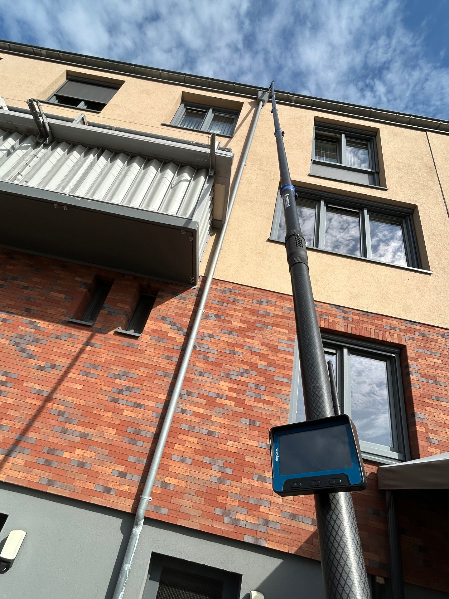 Telescoopstok met inspectiescherm reikt tot aan de dakgoot van een appartementencomplex