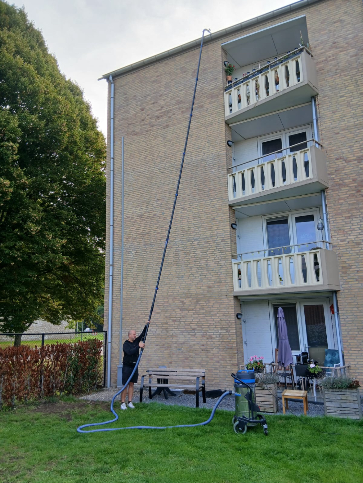GOOT-BUSTERS medewerker bedient de telescoopstok bij een appartementencomplex met balkons